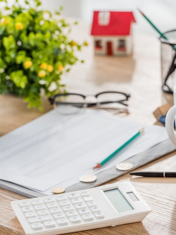 selective focus of calculator near coins, paper, glasses, green plant and house model on wooden